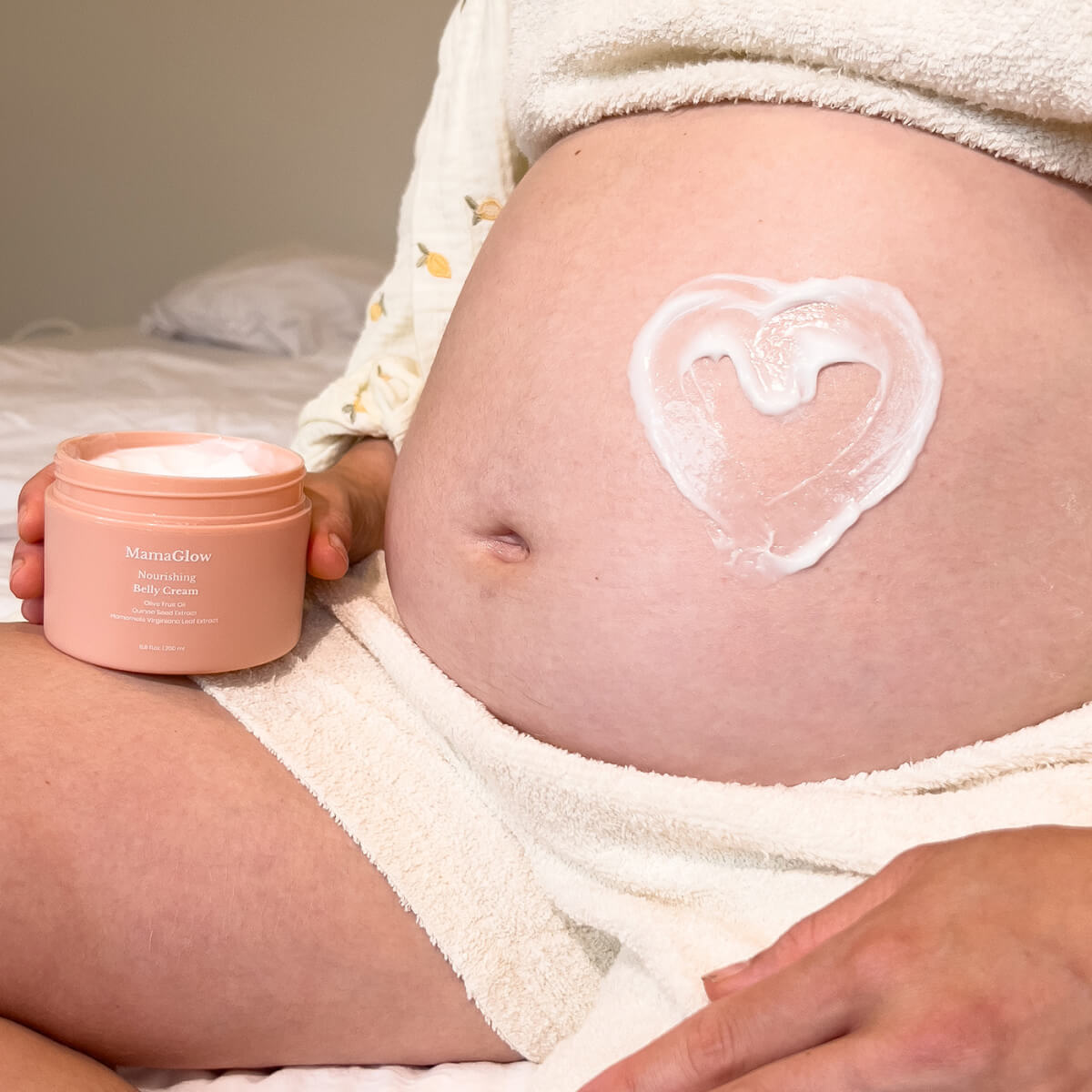 Pregnant woman applying cream to her belly in a cozy, decorated room.