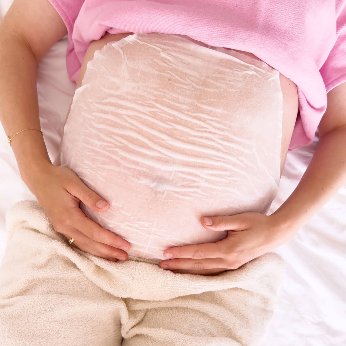 Pregnant woman applying cream to her belly in a cozy, decorated room.